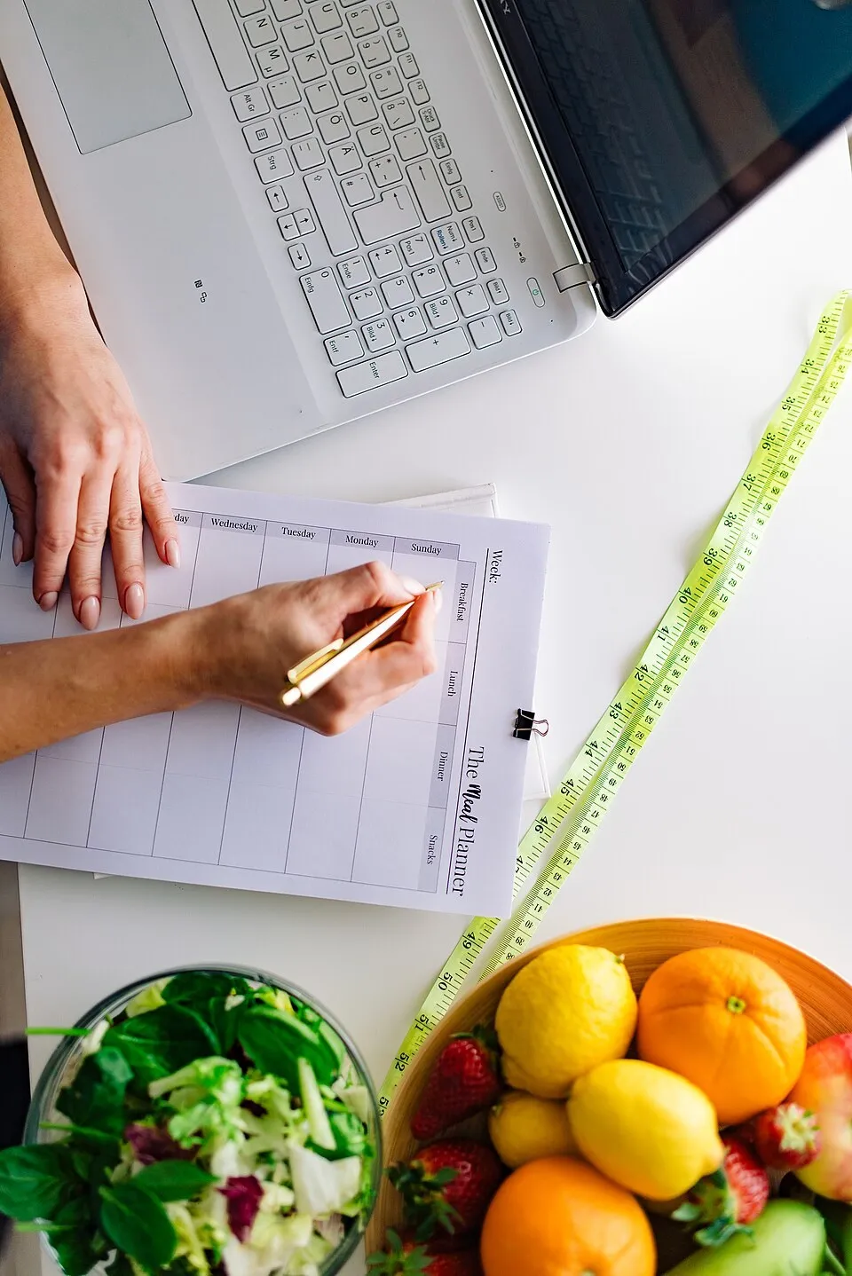 Planeamento de refeições numa folha semanal, com fruta, salada e fita métrica